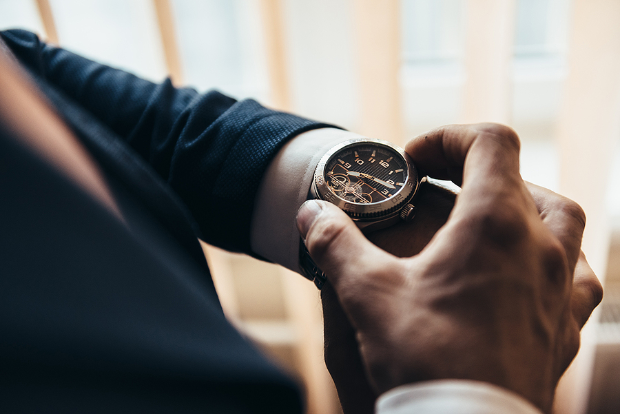 Your Guide to Choosing the Perfect Men's Watch a stylish mechanical watch on the arm of a man dressed in a blue jacket with a white shirt that watches the time on the clock holding the clock by hand