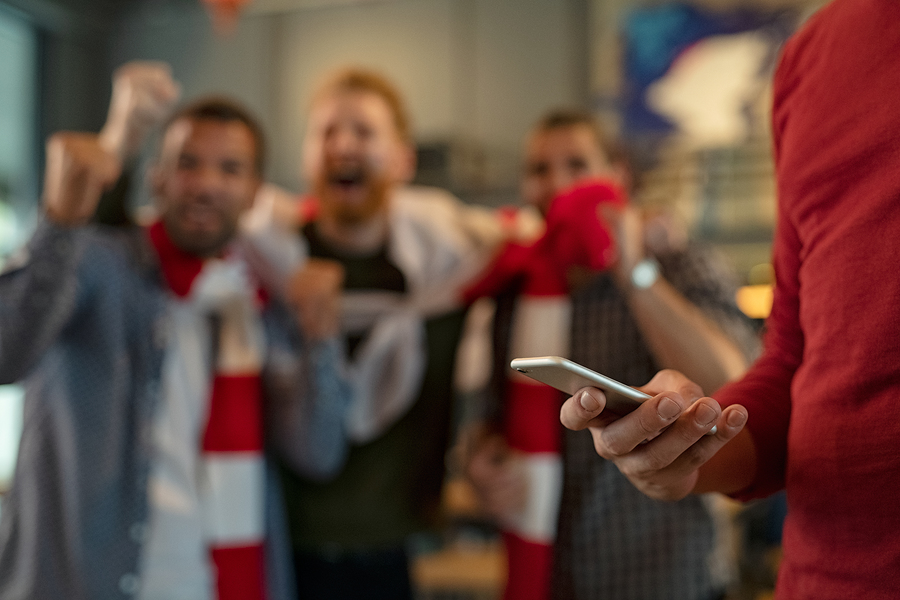 Close up of man holding smartphone and betting on the game while