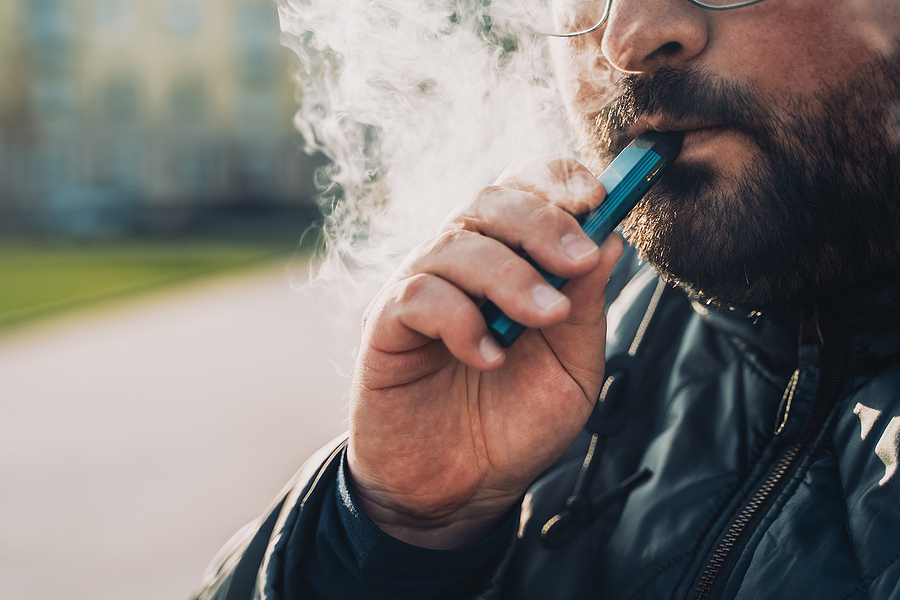 Man smokes new Vape Pod System, inhales and exhales vapor of electronic cigarette, vaping concept, selective focus, toned