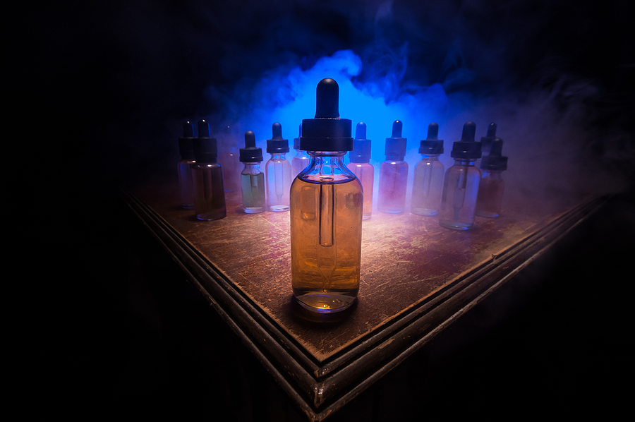 Vape Juices: What You Need To Know Smoke Clouds And Vape Liquid Bottles On Dark Background. Light E