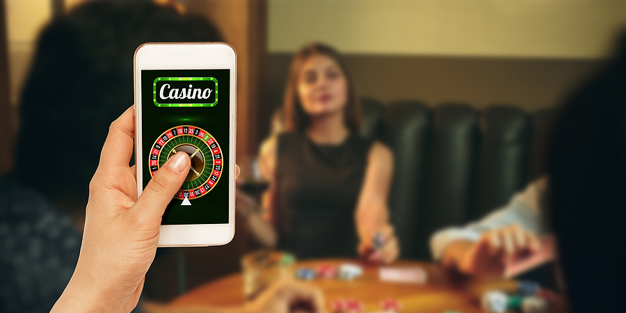 7 incredible things about online casinos Online gambling, casino concept. Hand holding device with lottery, casino cover. Playing dips and cards on table on the background. Poker, bookmaking, gaming, modern technologies, business and finance.