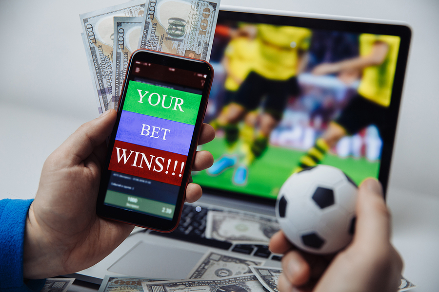 Sports Betting in Papua New Guinea – Is It Worth Your Time and Money? Smartphone with betting mobile application and males hand with soccer ball. Sport and betting concept