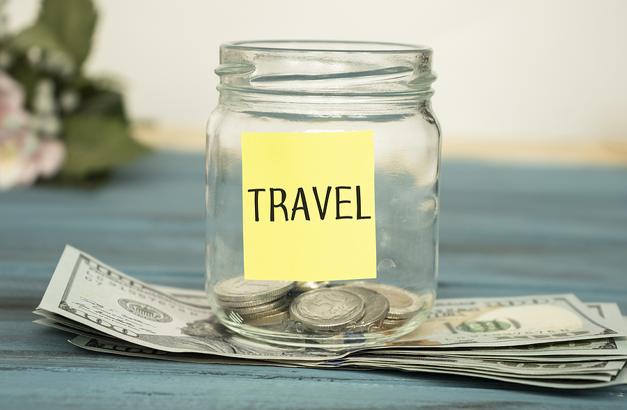 Travel budget - vacation money savings in a glass jar on world map. Travel budget concept. Money saved for vacation in glass jar on world map background, copy space. Banknotes and coins for adventure