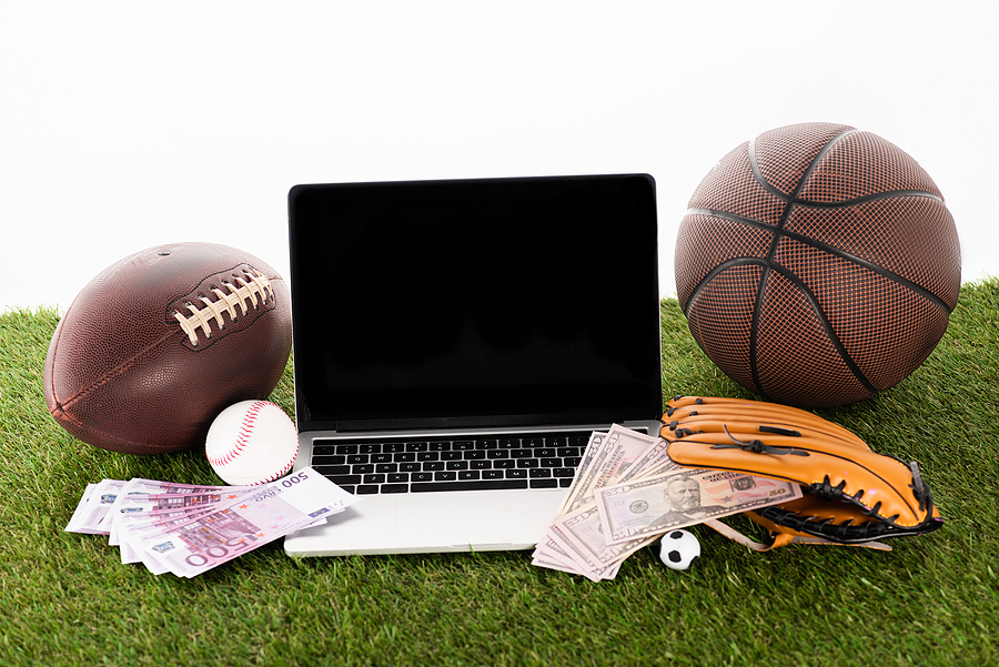 NFL, NHL, and MLB: What are the Best Leagues to Bet on? laptop near sports balls, baseball glove, euro and dollar banknotes on green grass isolated on white, sports betting concept