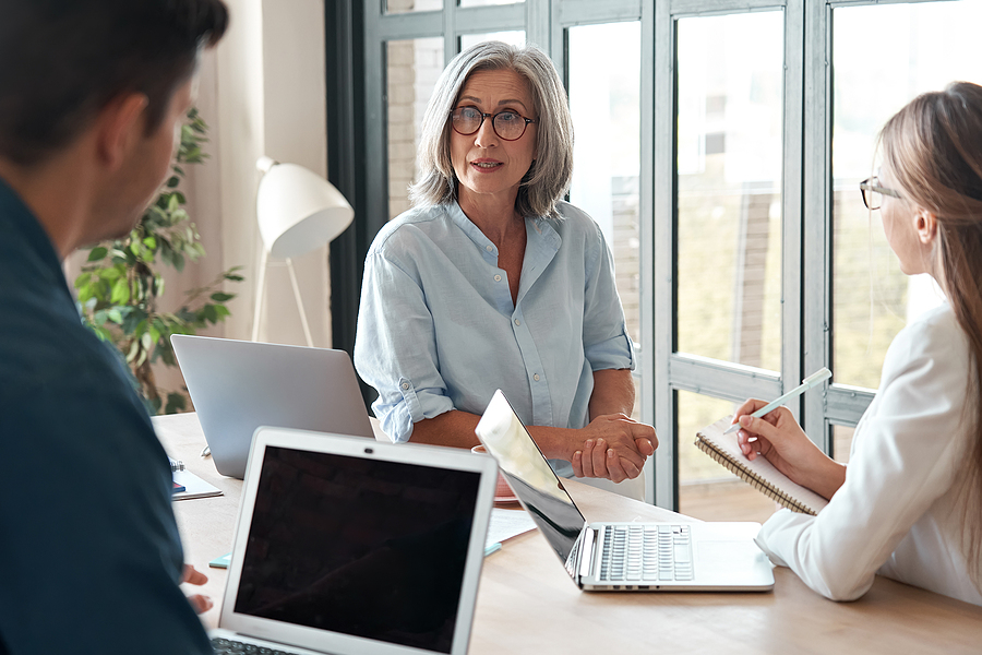 Mature old female mentor coach supervisor training young interns at group office meeting professional workshop. Middle aged business woman teacher professor working with students at university class.