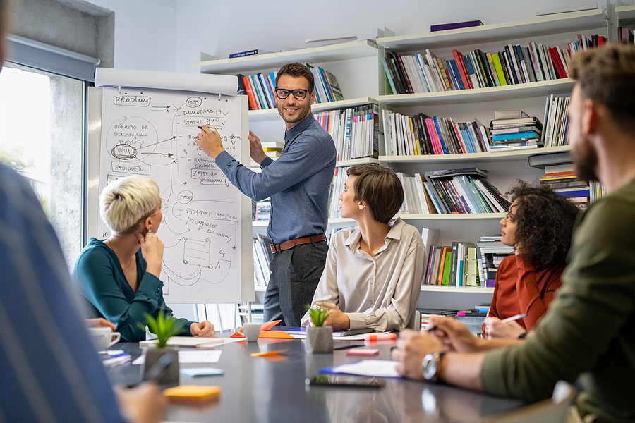 Confident businessman giving a presentation in casual office. Leader briefing his creative business team with annual goals. Mid business man training multiethnic businesspeople in conference room. Workplace.