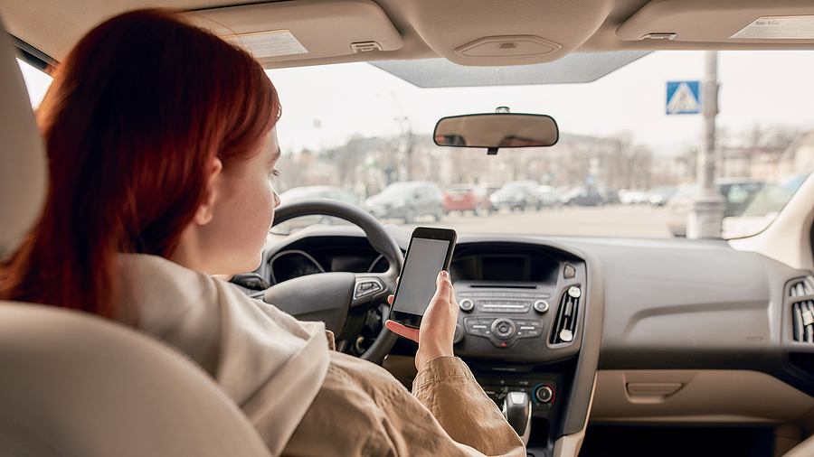 What Is Considered as Distracted Driving In Alberta? Distracted Young Female Driver Looking At The Screen Of Her Mobi