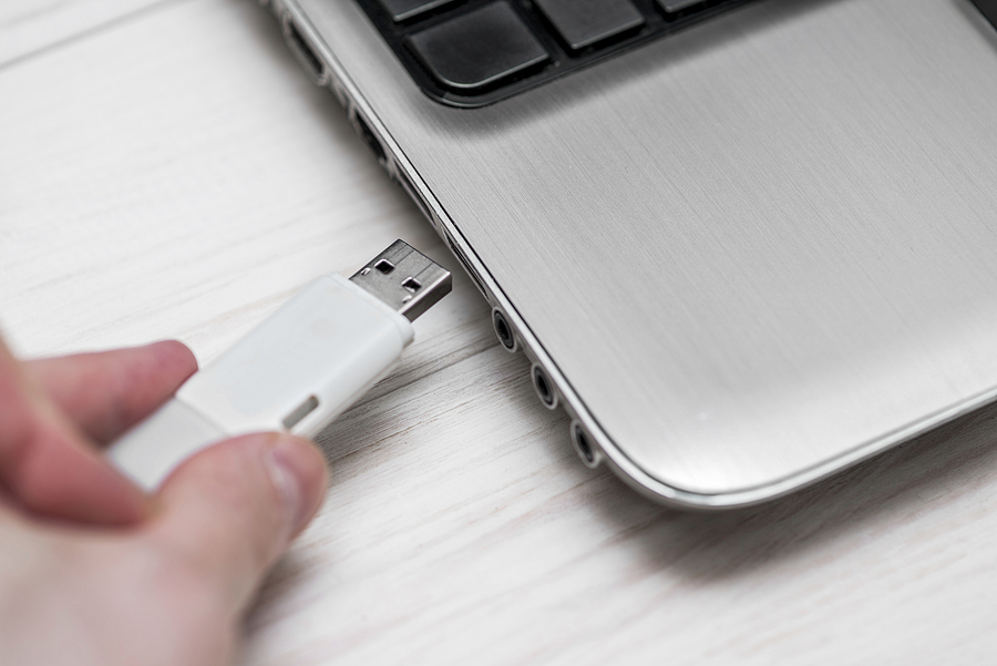 New Flash Drive Counters USB Cyber Threats Plugging removable flash disk memory into laptop USB slot. Man hand inserting USB flash drive into laptop computer on wooden white background. Copying data from flash drive to laptop computer storage