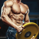 How Much Does a Bodybuilding Coach Cost? bodybuilding blonde brutal sexy strong bodybuilder athletic fitness man pumping up abs muscles workout bodybuilding concept background - muscular handsome men doing health care fitness exercises in gym naked torso