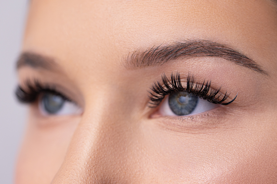 What Style of Eyelash Extensions Are Best For Me? eyelash extensions Close up portrait of woman face. Young, beautiful girl with fresh soft skin combing long black eyelashes with special mascara brush. Fake eyelashes. Eyelashes extensions close up