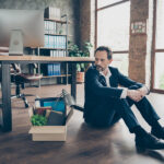 Photo of laid off dismissed sad worker mature guy fail fired agent loser lost job packed belongings look thoughtful box financial crisis sit floor wooden parquet workstation office indoors termination