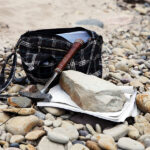 Want to Get Into Amateur Geology? Here's How to Start Geologists bag with the stones and notes papers and hammer. Geology science concept. The geologists hammer and mineral are laid out on a pebbels