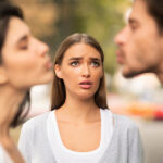 Best Things To Do When You Suspect Your Partner is Cheating Infidelity. Girl Looking At Her Cheating Boyfriend Kissing Dating With Other Woman In Park Outdoors. Selective Focus