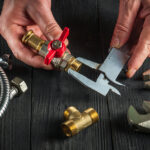 Plumber measures the size of fitting using a caliper before connecting water or gas pipe. Closeup of the hands of the master plumber in workshop.