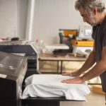 Professional graphic print technician work on digital t-shirt printing heat press machine in printing production shop