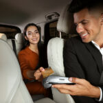 Young woman paying for service using credit card via payment terminal in modern taxi
