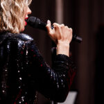 girl singer with microphone singing and dancing over holiday glowing background. Karaoke singer. Disco. Celebration