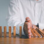 Risk and Strategy in Business, Hand stopping wooden block domino business crisis effect or risk protection concept, prevention and development to stability
