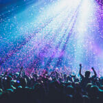 How much does it cost to be a superfan A crowded concert hall with scene stage lights, rock show performance, with people silhouette, colourful confetti explosion fired on dance floor during a concert festival