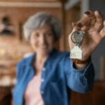 Household Tips for Elderly Homeowners Happy elderly female homeowner pose in country cottage hold keys