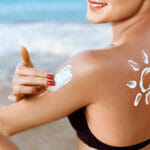 How to fall in love with sunscreen Woman Applying Sunscreen Cream On Tanned Shoulder. Skincare. Bod