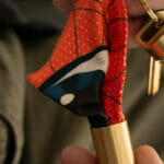 Person holding brass keyring capsule with orange glasses cleaning cloth tucked inside