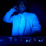 Can I Make a Living as a DJ? African-American DJ puts on music in a dark room. Color music for a party. DJ wearing headphones and glare sunglasses puts on music at a party.