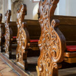 Empty pews inside church close-up, carved wooden pews in catholic cathedral, detail of Christian church interior. Beautiful old pews, worship benches in sanctuary. Prayer, faith and service concept.