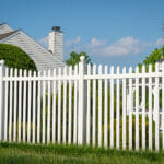 White vinyl fence in a cottage village tall thuja bushes behind the fence fencing of private property grass plastic