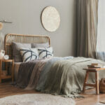 Stylish composition of bedroom interior with wooden bed, furniture, dried flowers in vase, rattan decoration and elegant accessories. Beautiful bed sheets, blanket and pillows. Cozy home decor.