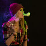 Vaping girl. Young hipster woman vape e-cig on black background. Hip-hop style. Studio shot