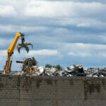 Crane With Grapple Dropping Scrap Metal On Mountains Of Scrap An