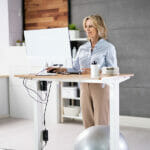 What are the Health Benefits of Standing Tables? Woman Using Adjustable Height Standing Desk In Office For Good P