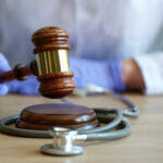 Close-up of woman doctor hands in gloves striking with judge gavel. Medical malpractice, personal injury lawyer and healthcare legal aspects concept