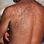 man with a very hairy back standing outside by a river on a hot