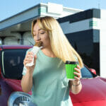 Our Top Favorite Gas Station Restaurants in American Beautiful Young Woman With Coffee Eating Hot Dog Near Car At Gas