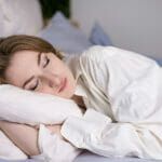 Raven Dream Meaning. Calm serene beautiful young lady wears pajamas, lying down in a dream, relaxing sleep in a cozy white bed on a soft pillow covered with a blanket, enjoying a good healthy sleep concept, top view