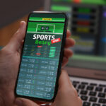 Man Betting On Sports Using Smartphone And Laptop At Table, Clos