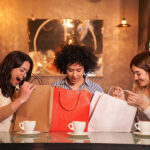 Three Multiracial Friends In Bar-cafeteria Making Gifts For Birt