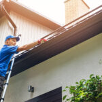 Thorough Gutter Cleaning to Ensure Proper Drainage and Protection Man On Ladder Cleaning House Gutter From Leaves And Dirt