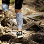 athlete runner runs rocks in mountain. closeup of legs compression socks and sneakers